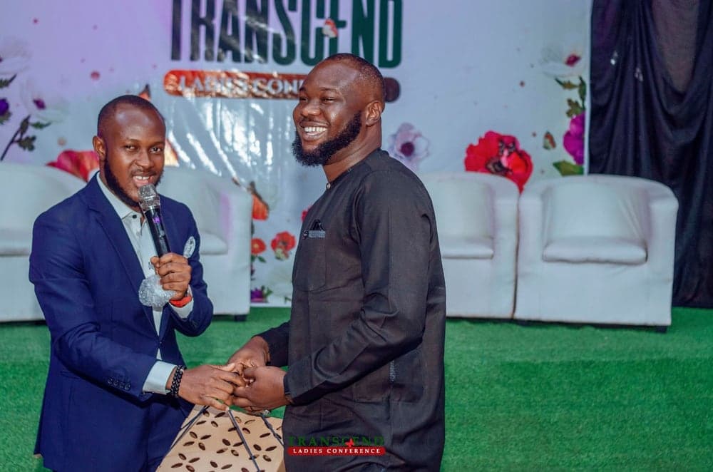 Two men sharing a warm moment on stage at the Transcend Ladies Conference, one holding a microphone and the other receiving a gift bag