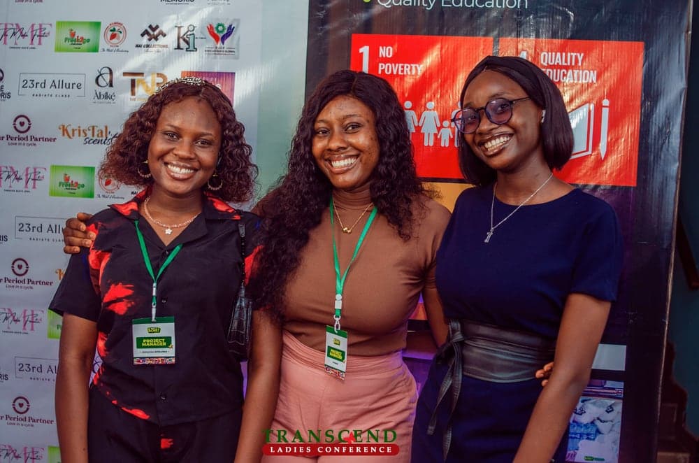 Three women wearing project manager passes in front of a Sustainable Development Goals banner at a ladies conference